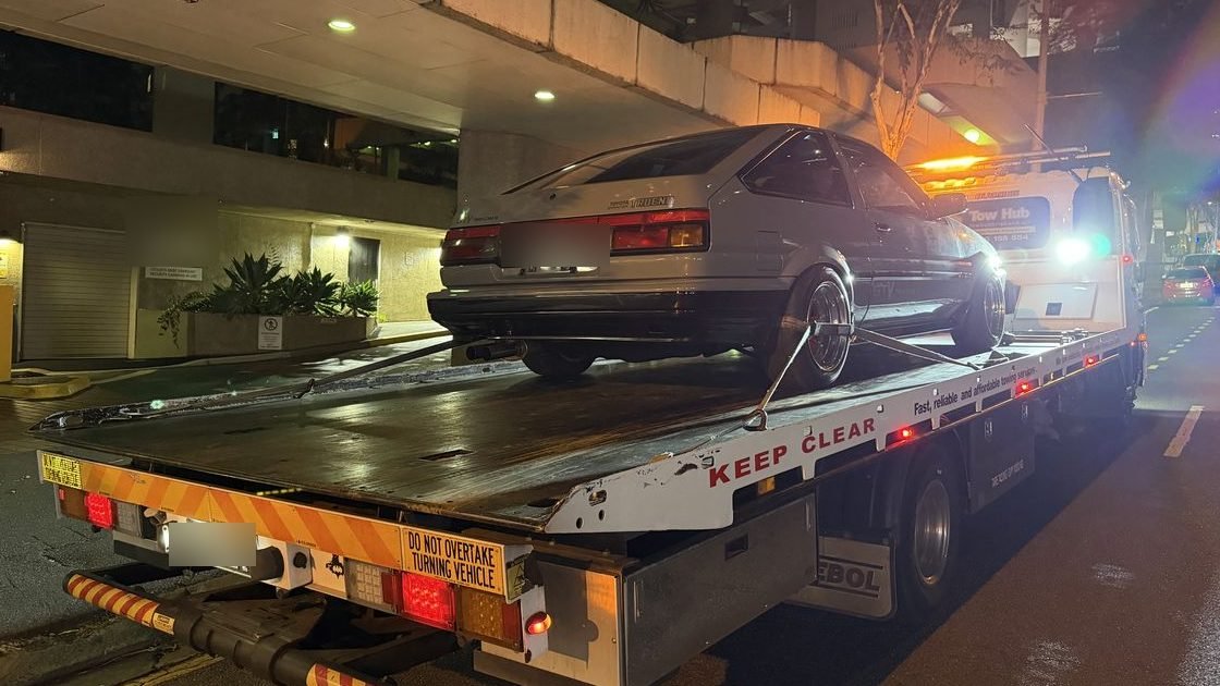 Flatbed tow truck loading a car downtown at night under streetlights